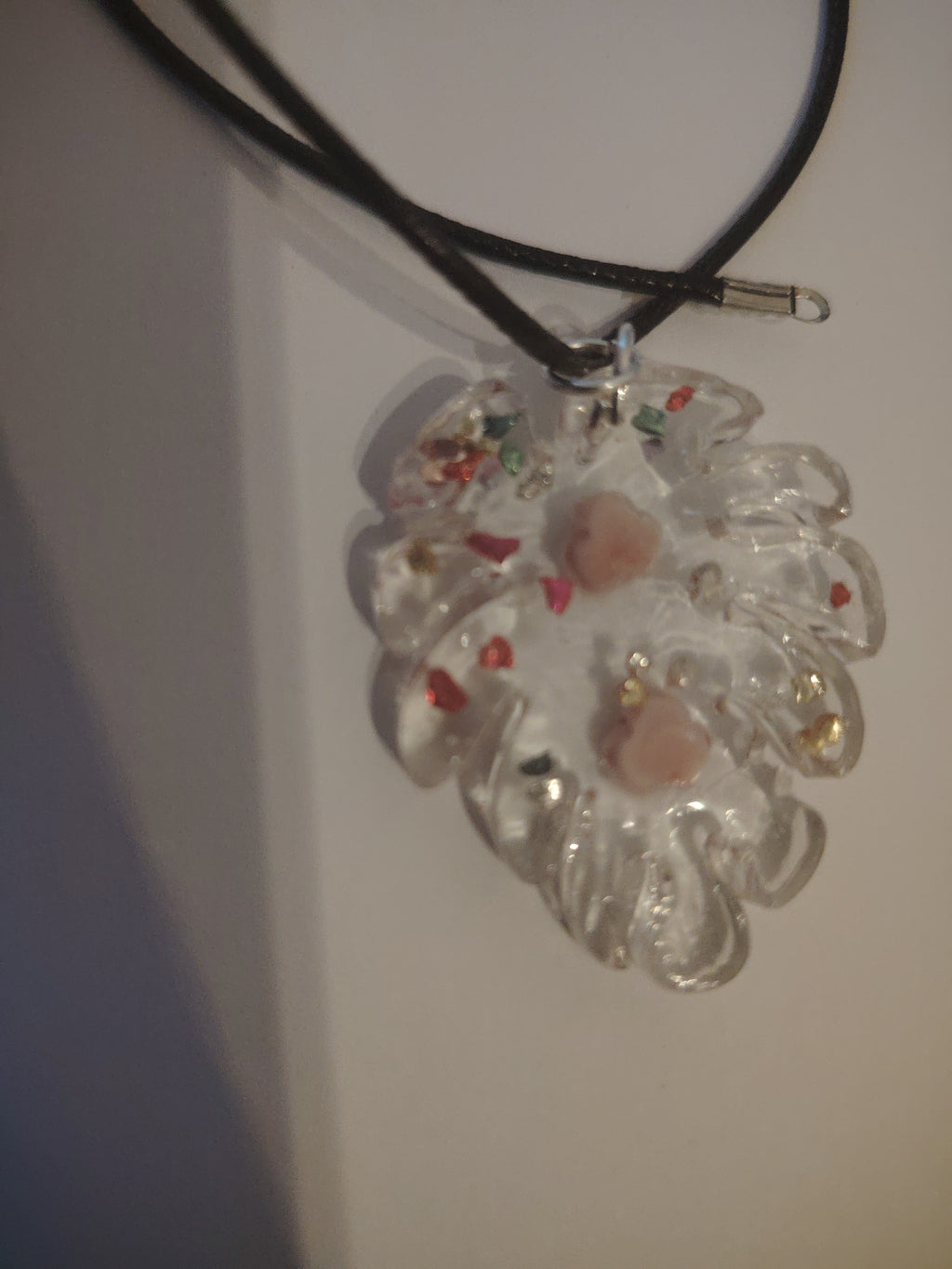 Pendant necklace made of cast UV resin in the shape of a leaf. Filled with two roses and colorful glitter stones.