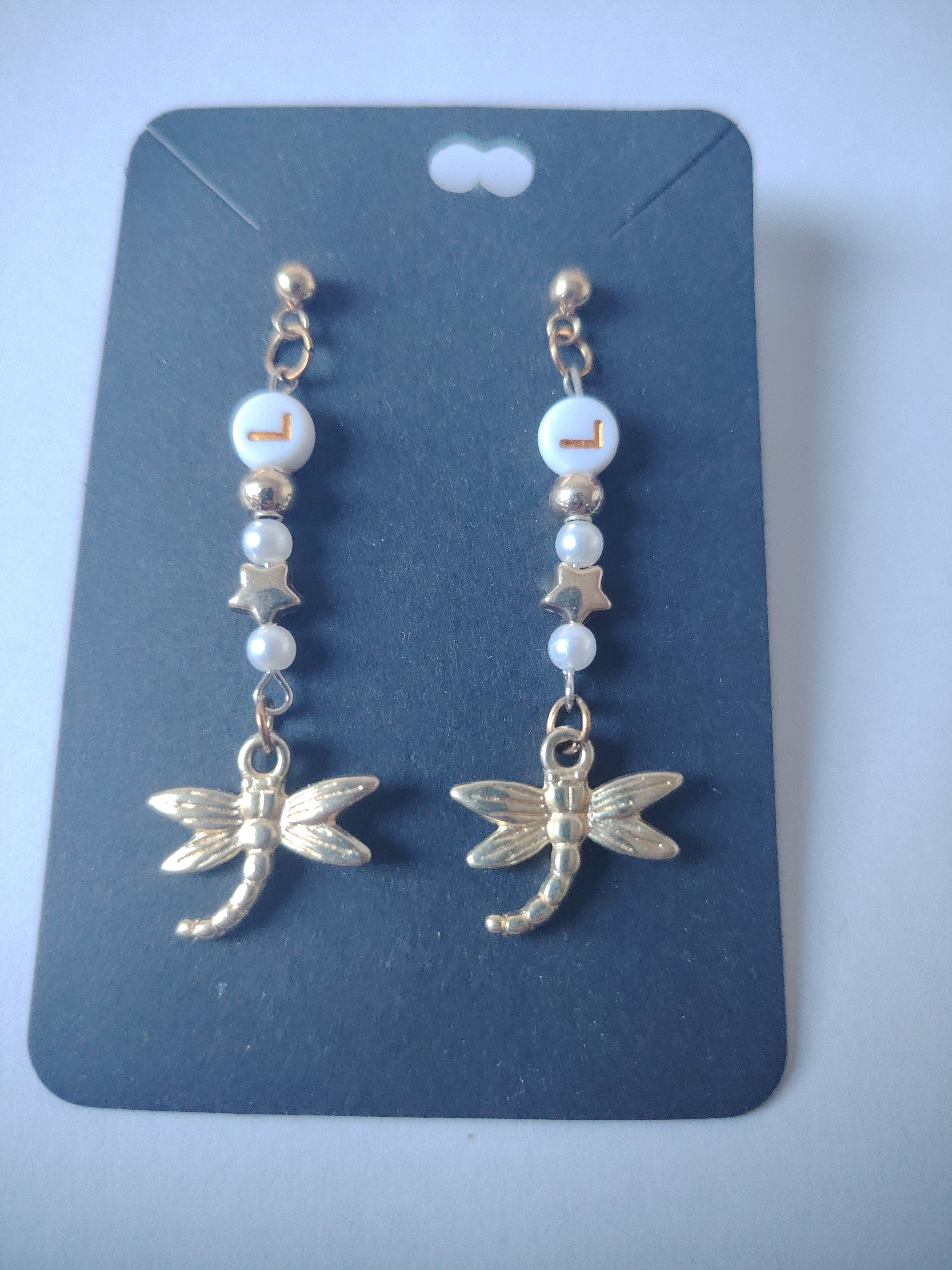 Earrings with a pretty dragonfly and the letter L (symbolizing the dragonfly) with small gold and white stars and pearls.