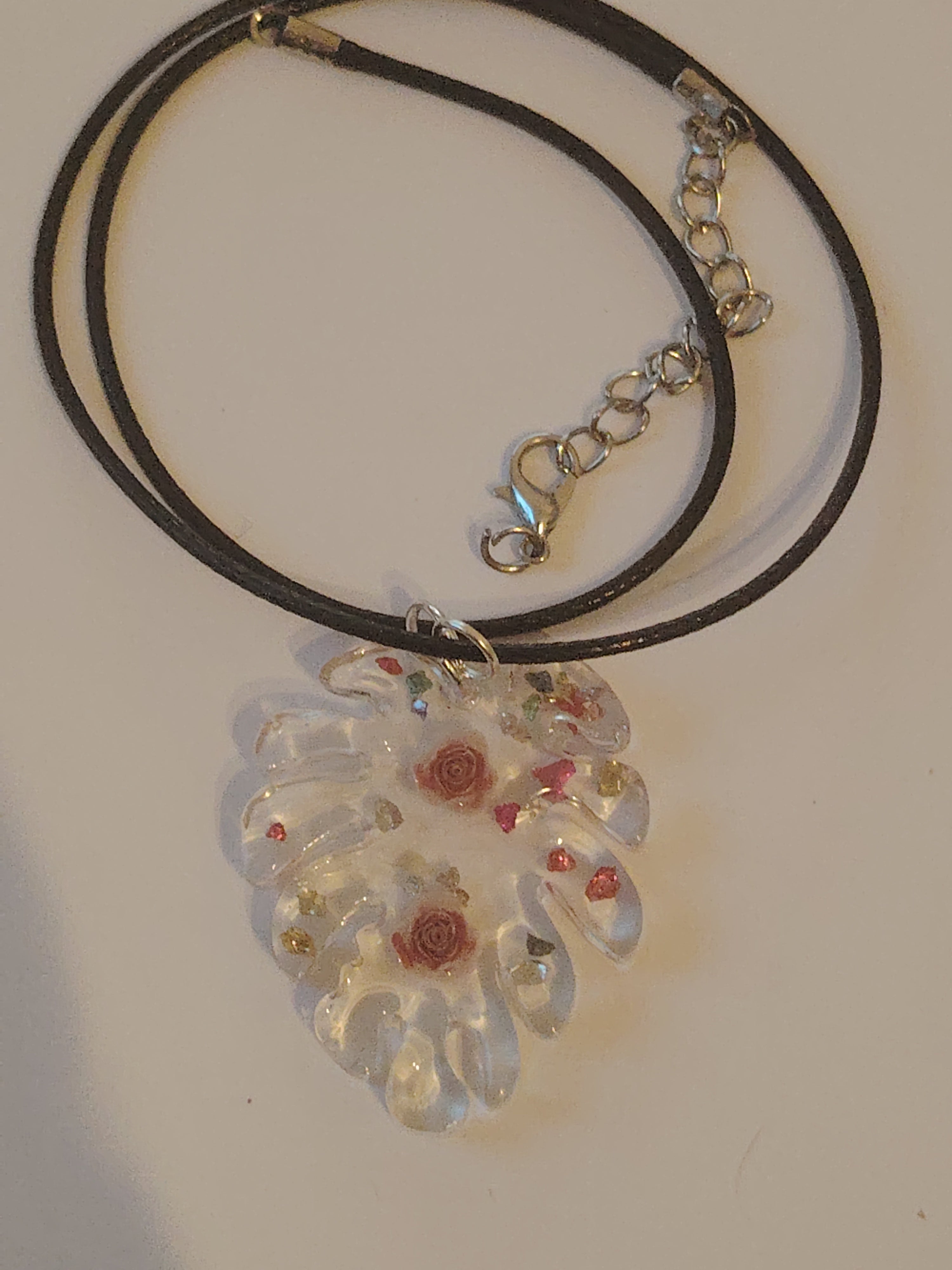 Pendant necklace made of cast UV resin in the shape of a leaf. Filled with two roses and colorful glitter stones.