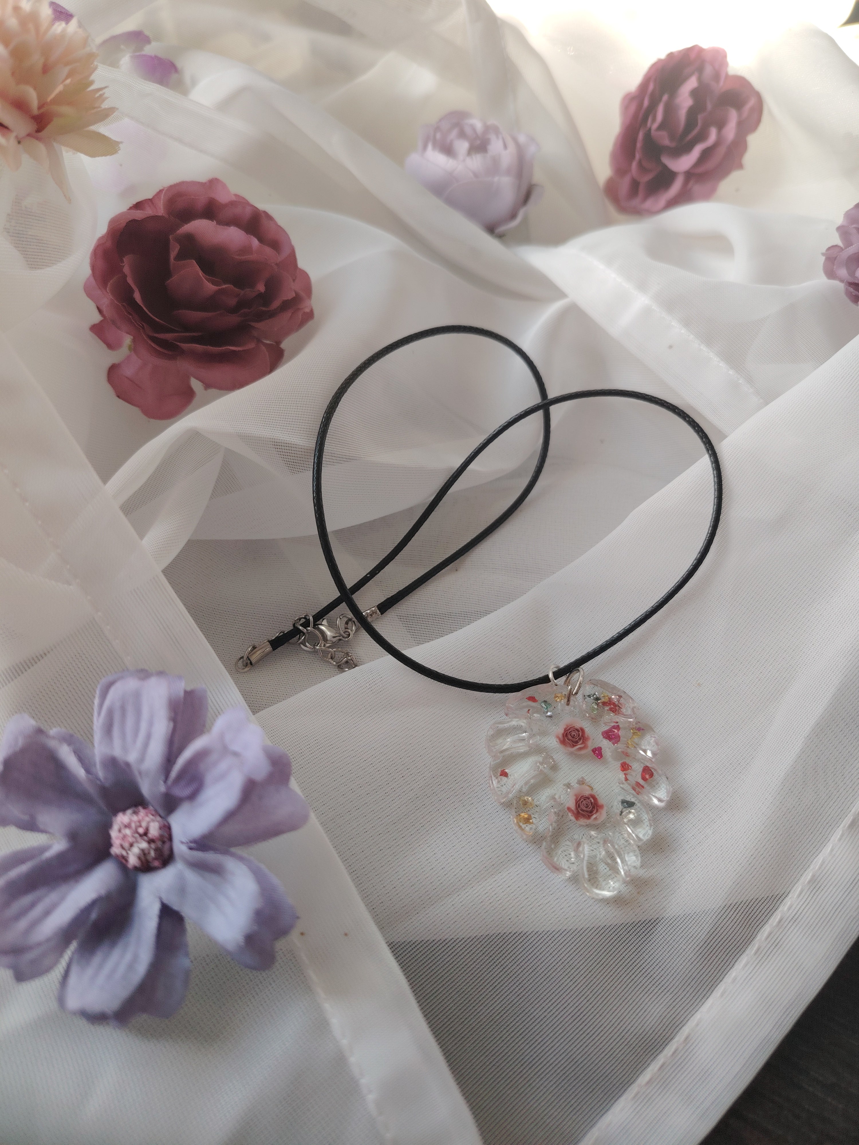 Pendant necklace made of cast UV resin in the shape of a leaf. Filled with two roses and colorful glitter stones.
